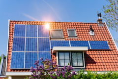 Solar panel on a red roof reflecting the sun and the cloudless blue sky